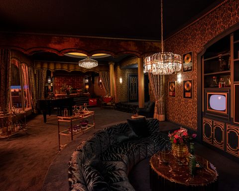 a dimly lit carpeted room with a sunken black sofa and a shimmering chandelier above