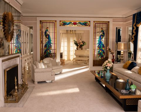 a living room with white seating with colorful stained glass windows depicting peacocks