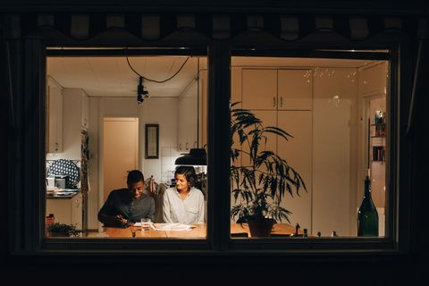 mother assisting son in studying at home seen through window