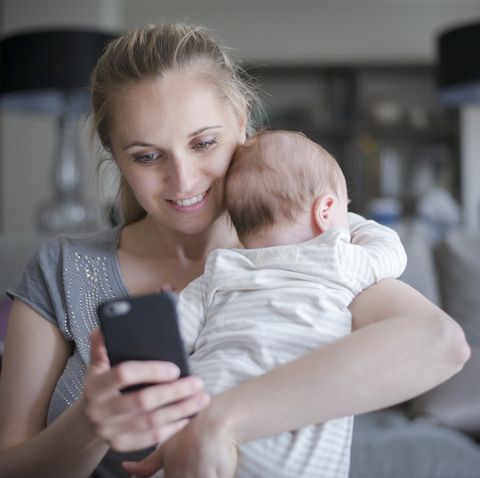 madre con bebé en brazos y móvil escribiendo