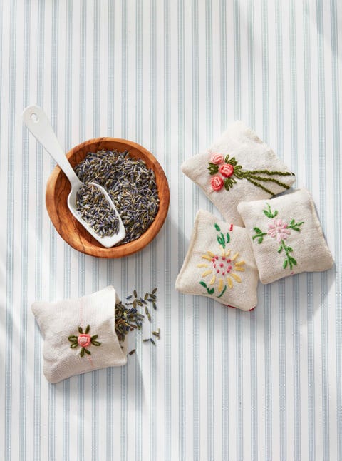 four small linen sachets embroidered with flower designs beside a bowl of dried lavender and a scoop
