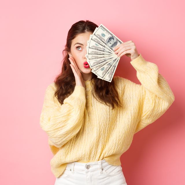 una mujer sujeta un fajo de billetes de dólar delante de un fondo rosa