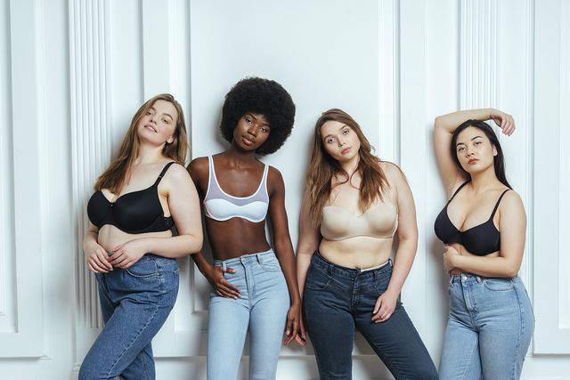 multiethnic group of female models wearing bras and jeans posing against wall