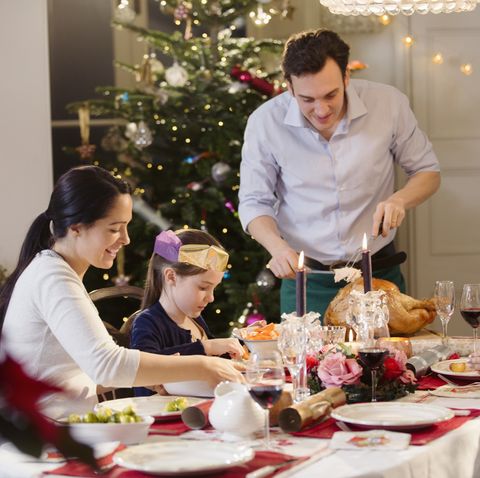 Multi-generation family carving Christmas turkey at candlelight dinner table