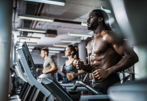 Muscular build black man warming up on treadmill in a health club.