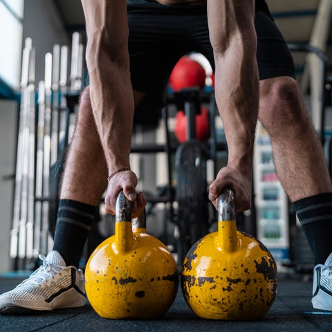 muscular male athlete holding kettlebells in gym