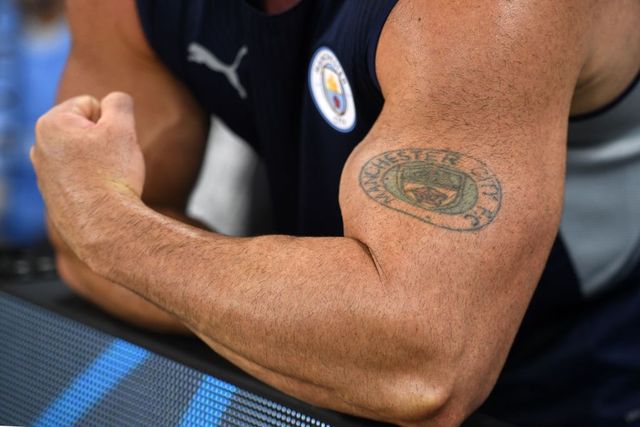 un hombre muestra un tatuaje en su bíceps mientras saca músculo