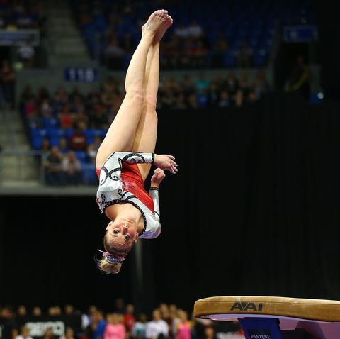 mykayla skinner in midair over the vault in a red sparkly leotard and bow in her bun