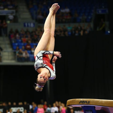 mykayla skinner in midair over the vault in a red sparkly leotard and bow in her bun