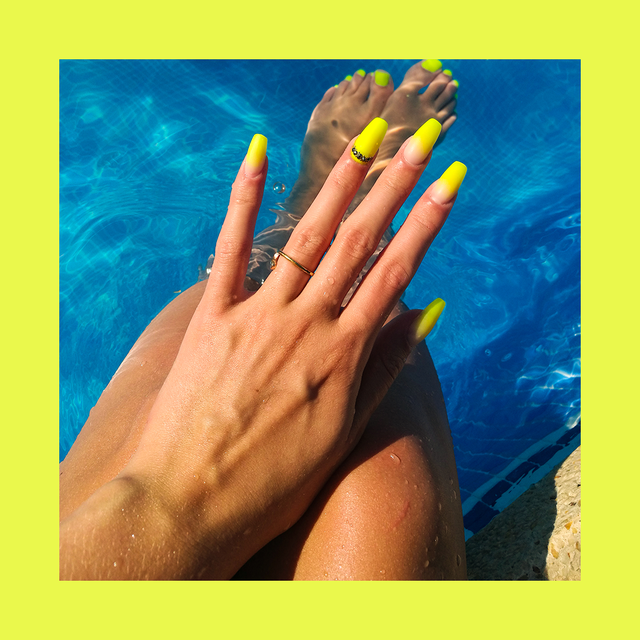 person in pool showing off yellow acrylic manicure