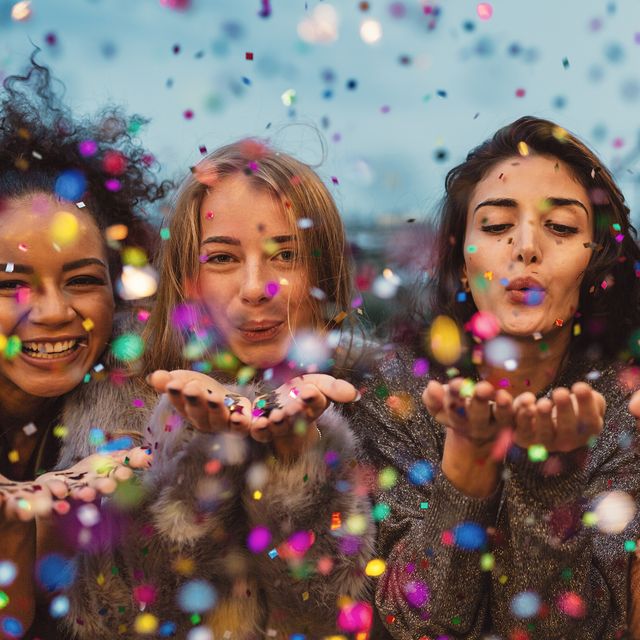 Young women blowing confetti from hands.