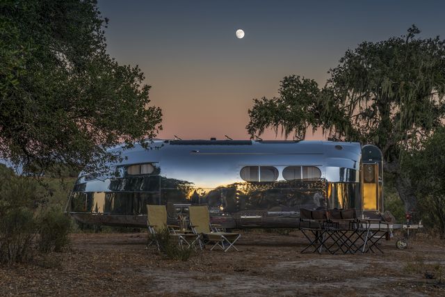 bowlus camping trailer parked at campsite with chairs out front and a sunset in the background