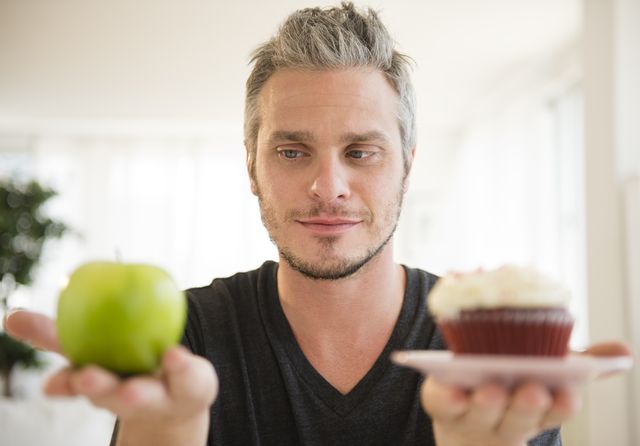 usa, new jersey, jersey city, man weighing green apple against cup cake