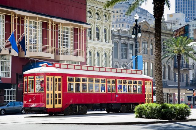 new orleans bright red streetcar traveling amid palms and flags