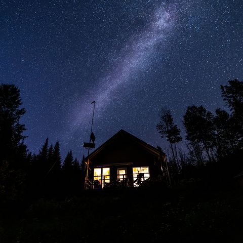 night sky and milky way nature panorama behind a beautiful tiny house or chalet in the forest