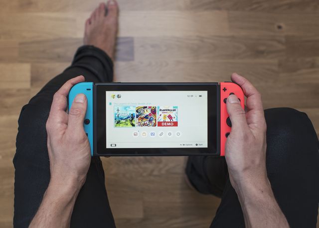 gothenburg, sweden   march 10, 2017 a shot from above of a young mans hands holding a neon coloured nintendo switch video game system developed and released by nintendo co, ltd in 2017 the system is turned on and its main menu is showing on the display shot on a hardwood floor background in a home environment