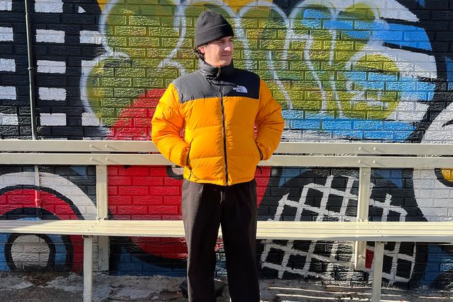 man wearing a beanie and puffy winter jacket standing in front of a graffiti wall