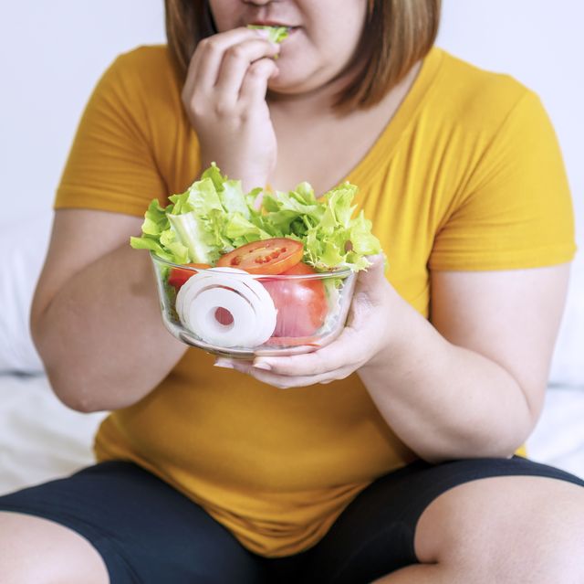 obesity young women eat green organic vegetables while sitting on the white bed fat female holding bowl salad vegetarian while eating lettuce in her hand concept food good healthy for weight loss