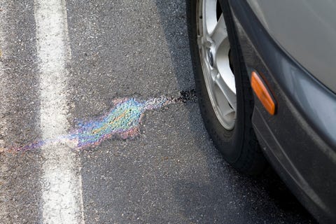 Oil spot on asphalt next to car wheel