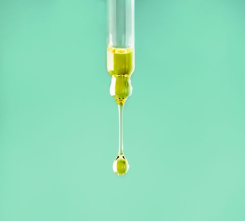 Oily drop falls from a cosmetic pipette on the light background. Skin care. Essential oil or water dropping Minimalism