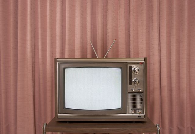 old television on stand, in front of curtain