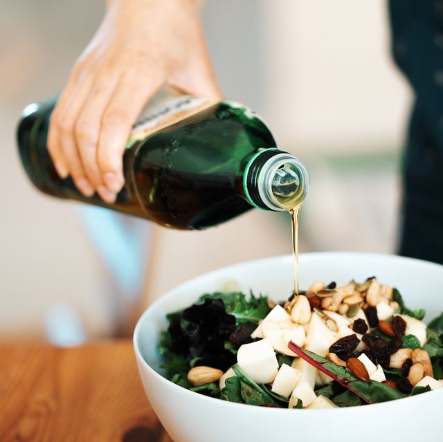 person pouring olive oil on salad