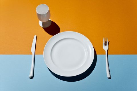 what is the omad diet   shown by a high angle view of white glass, fork, knife and plate on a colored table