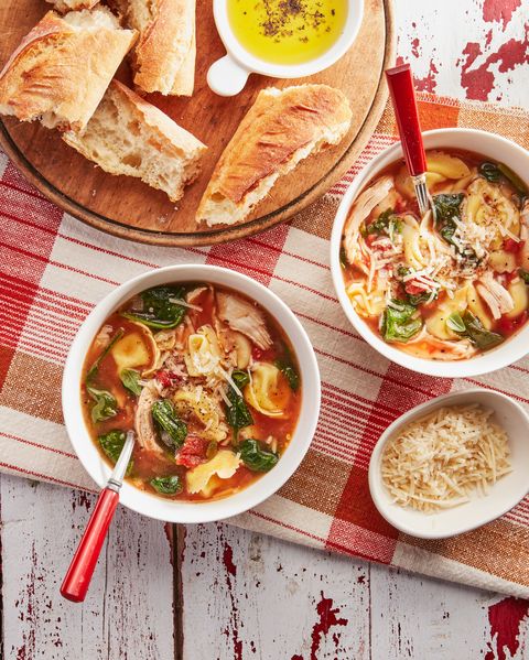 chicken tortellini soup in two bowls with spoons and a small bowl of shredded cheese and pieces of bread for serving