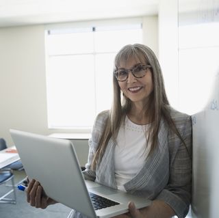 Portrait professeur souriant avec ordinateur portable au tableau blanc en classe