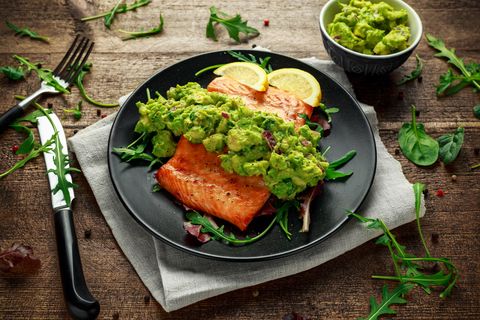 Oven cooked salmon steak, fillet with avocado salsa and green on black plate. wooden table. healthy food
