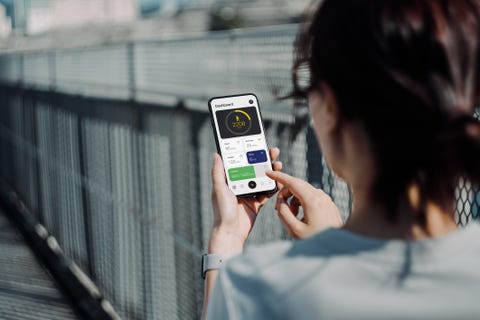 Over the shoulder view of young Asian sports woman using fitness app on smartphone to monitor her training progress while doing outdoor walk / exercising in the fresh bright morning with shades of sunlight over the shoulder view of young asian sports woman using fitness app on smartphone to monitor her training progress while doing outdoor walk exercising in the fresh bright morning with shades of sunlight