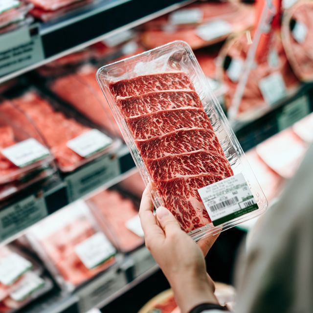 over the shoulder view of young woman choosing meat and holding a packet of organic beef in front of the refrigerated section