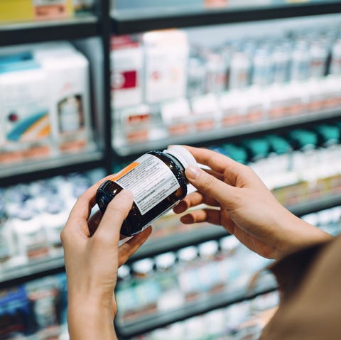 over the shoulder view of young asian woman browsing through medical products and reading the label on a bottle of medicine in front of the shelves in a pharmacy