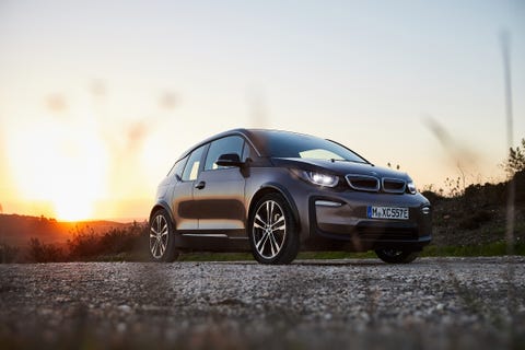 bmw i3 parked on pavement in front a meadow with a sunset in the background