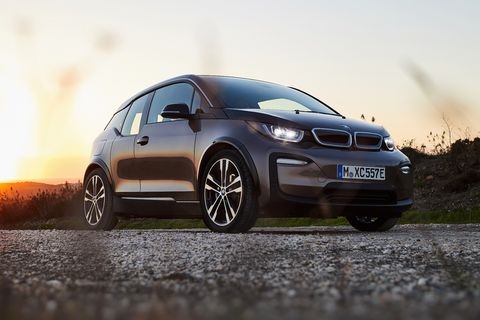 bmw i3 parked on pavement in front a meadow with a sunset in the background