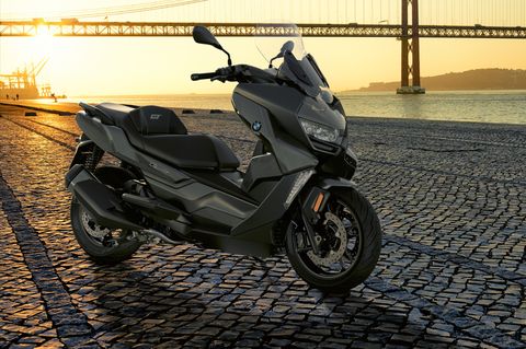 bmw c 400 gt motorcycle parked in front of a bridge in the distance with sunset in the background