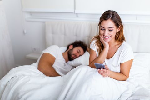cheating wife beautiful woman chatting privately on cellphone, hiding from her sleeping husband, empty space cheating girlfriend chatting on phone while boyfriend sleeping in bedroom at night