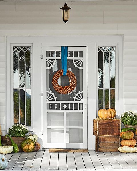 pecan shell wreath hung with blue ribbon on a porch decorated with mums, pumpkins and other fall gourds