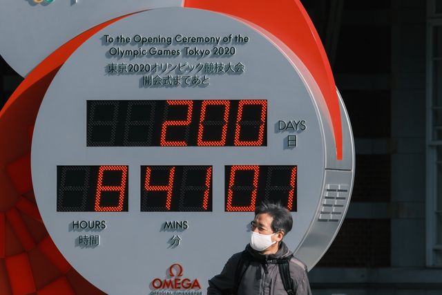 un hombre pasa en mascarilla por delante del reloj que marca la falta de 200 días para los juegos olímpicos de tokio 2021