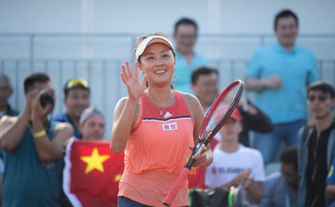 peng standing in front of a chinese flag wearing an orange tennis outfit waving