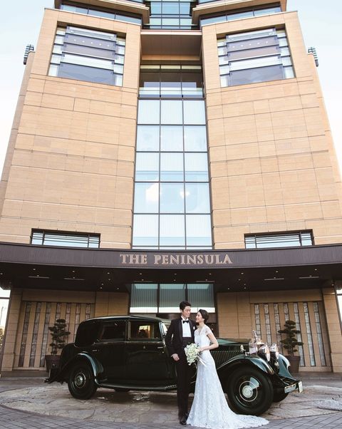 「ザ・ペニンシュラ東京」の外観の前にロールス・ロイスと一緒に佇む新郎新婦の写真。