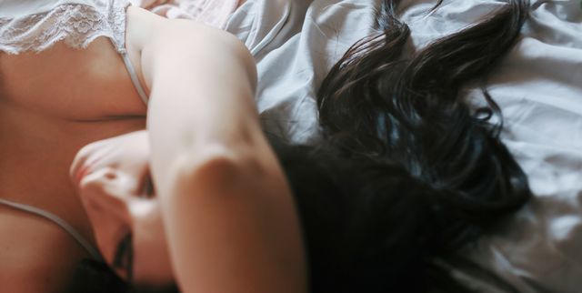 pensive brunette girl with hair forming a heart lying on the bed