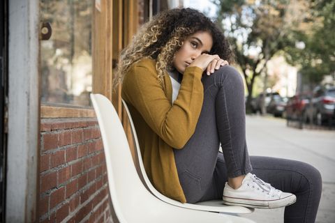 Pensive Mixed Race woman sitting on chair in city