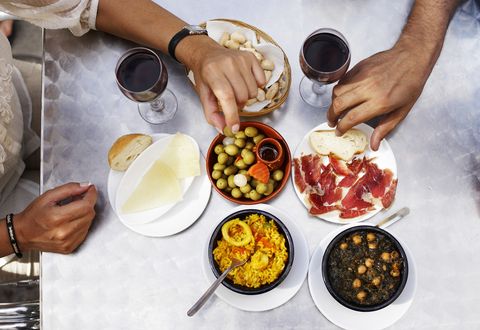 People eating tapas at outdoor restaurant, close-up of hands, overhead view
