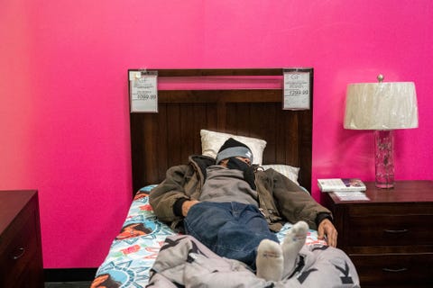 a man in a beanie takes a nap on a wooden bed at gallery furniture store in houston, which transformed into a warming station and opened its doors to cold texans who lost power