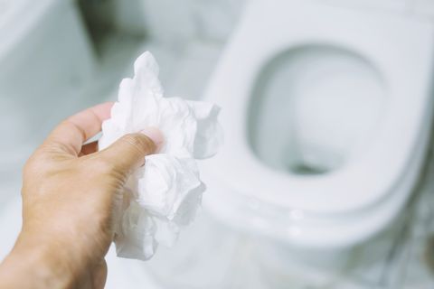 close up hand holding a tissue to be thrown into the toilet bowl can not drain water of toilet paper in the toilet bowl cause the stool to clog up
