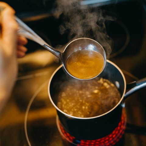 personal perspective of a hand holding a ladle while cooking a pot of soup