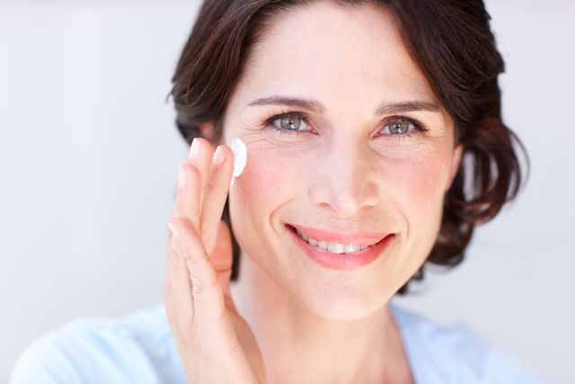 a mature woman rubbing moisturizer on her face