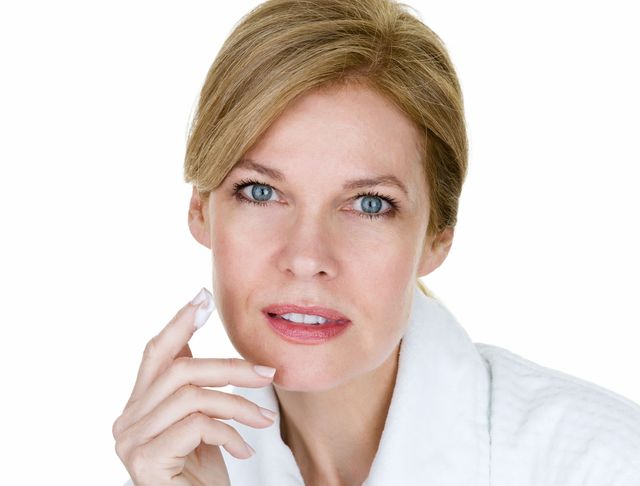 middle age woman wearing a bathrobe while applying moisturizer