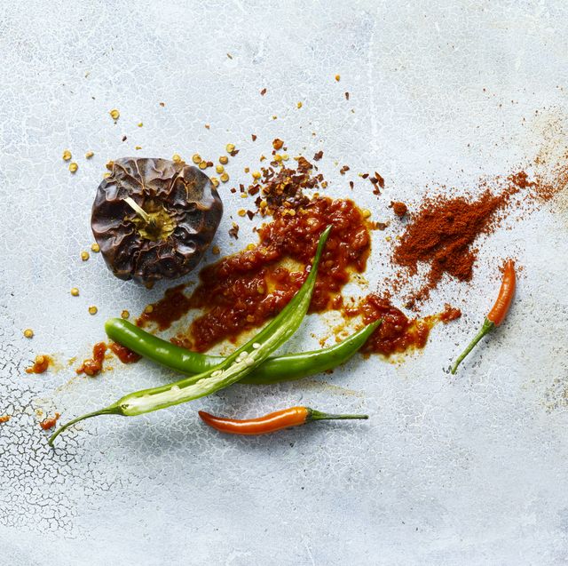 A pile of fresh peppers, dried peppers, hot sauce and ground pepper on a light background.
